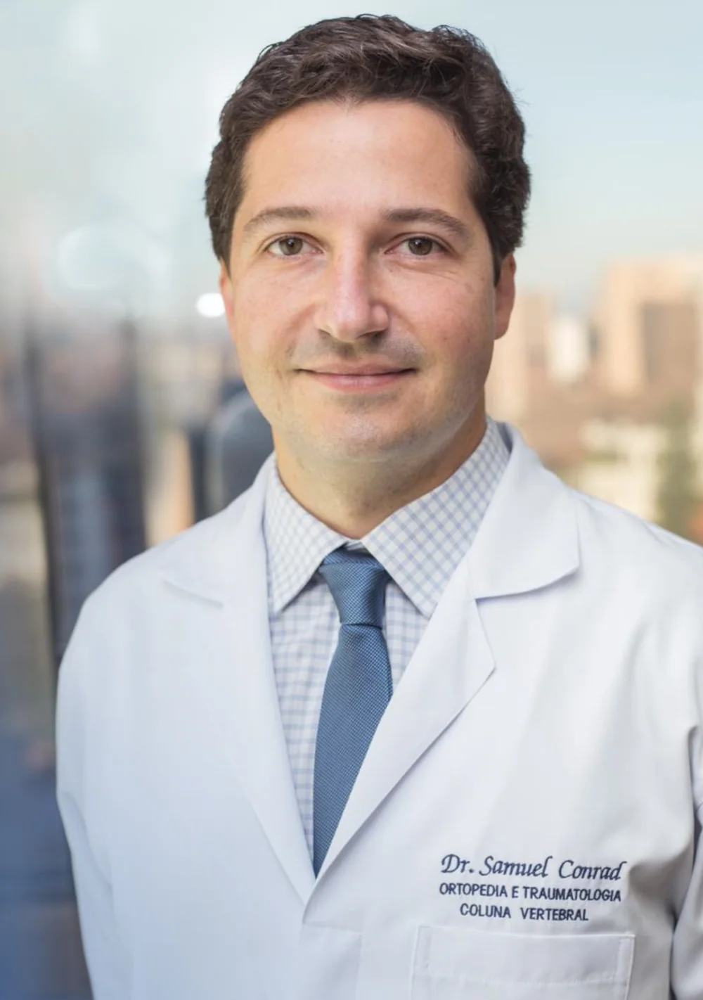 Dr. Samuel Conrad de jaleco, em pé, no consultório