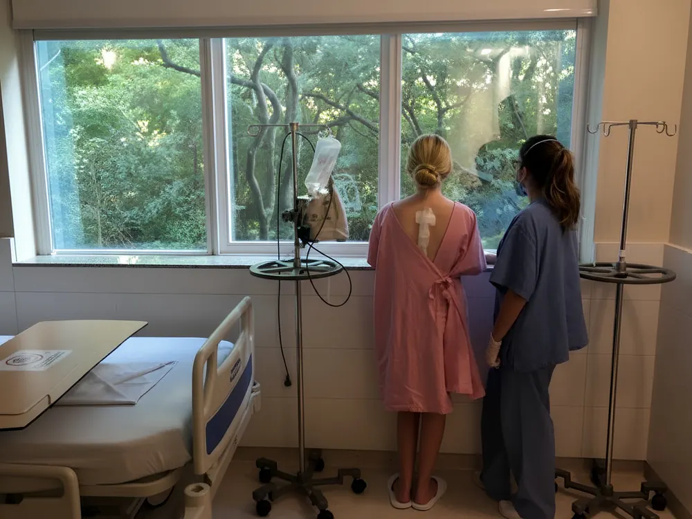 Paciente em pé no quarto do hospital, acompanhada pela equipe